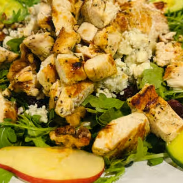 Close-up of a grilled chicken salad with blue cheese, greens, and apple slices.