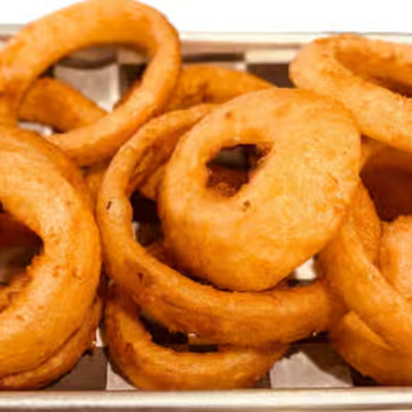 A close-up of golden-brown, crispy onion rings served in a metal basket with checkered paper.