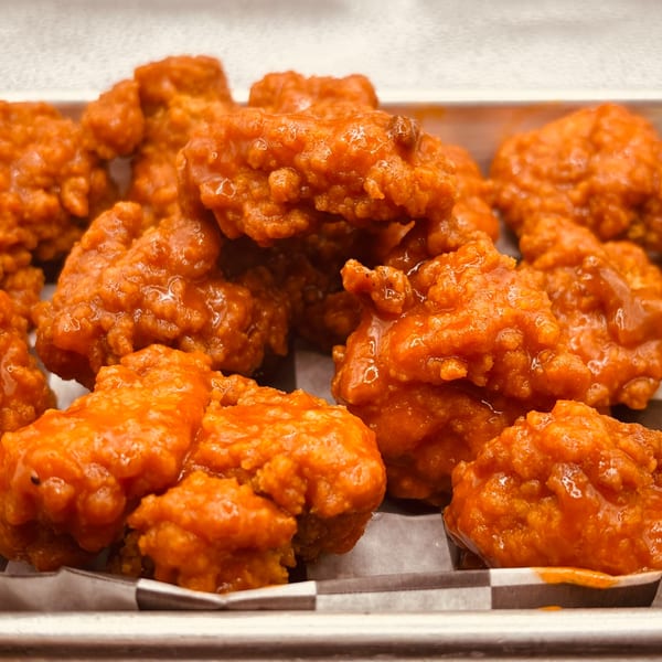 Close-up of Endzone Bar & Grill's boneless wings, coated in a vibrant orange sauce, served in a metal tray.