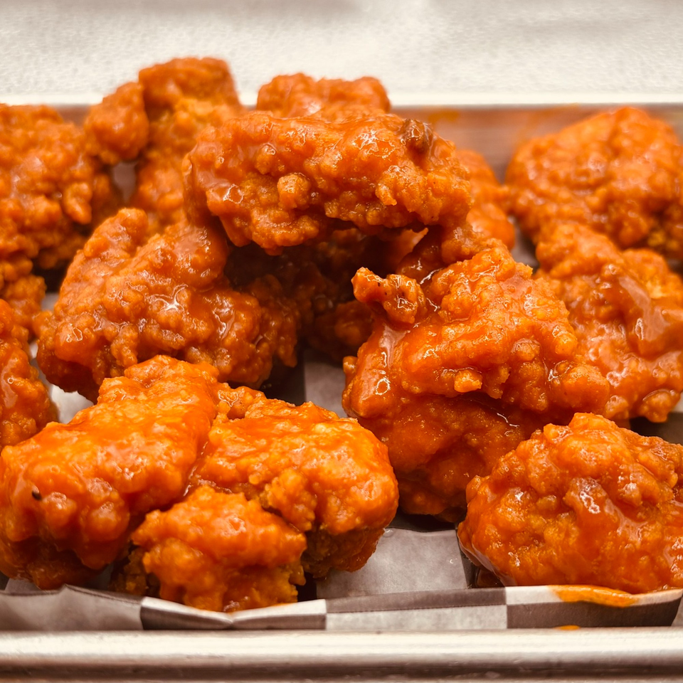 Close-up of Endzone Bar & Grill's boneless wings, coated in a vibrant orange sauce, served in a metal tray.
