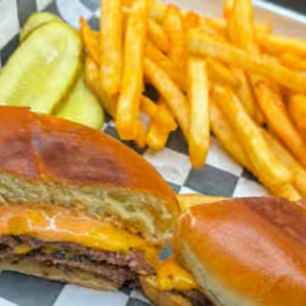 Cheeseburger with two patties, melted cheese, and pickles, served with golden french fries.